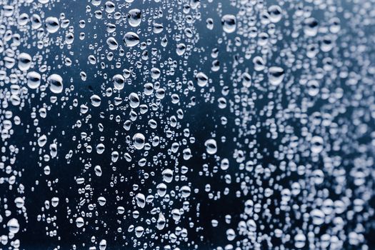 Close-up of clear water droplets on a dark glass background, conveying freshness.
