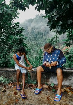 Two men sitting on a concrete bench in a foggy forest setting, dressed in casual wear.