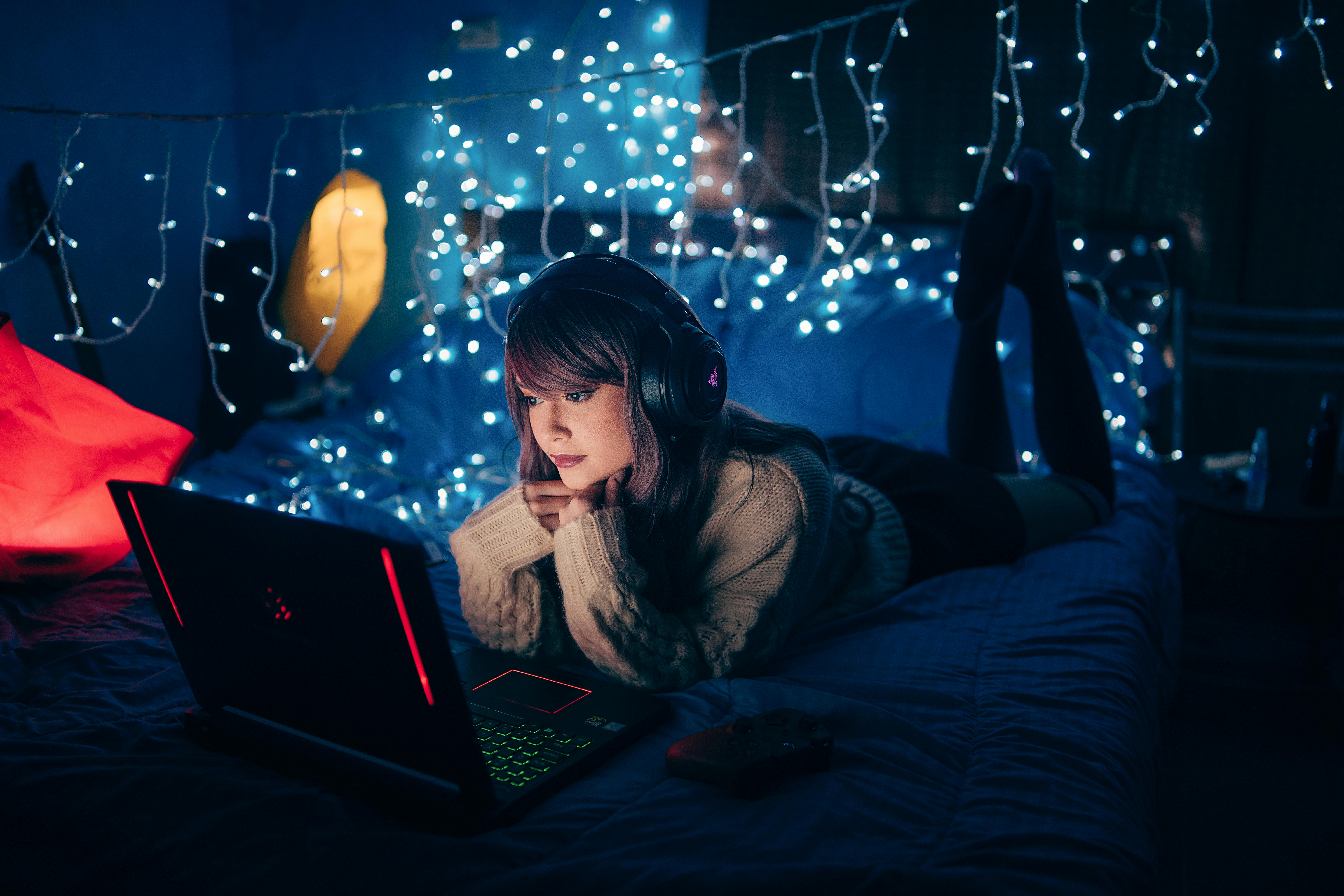 woman in brown sweater lying on bed with laptop