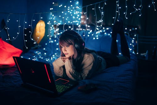 Free Woman in Brown Sweater Lying on Bed with Laptop Stock Photo