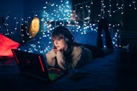 一名年轻女子在舒适的房间里，戴着耳机，使用笔记本电脑，周围环绕着温暖的童话般的灯光