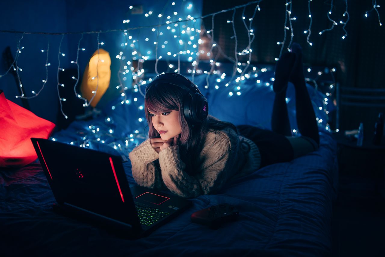 a young woman in a cozy room wearing headphones and using a laptop sur