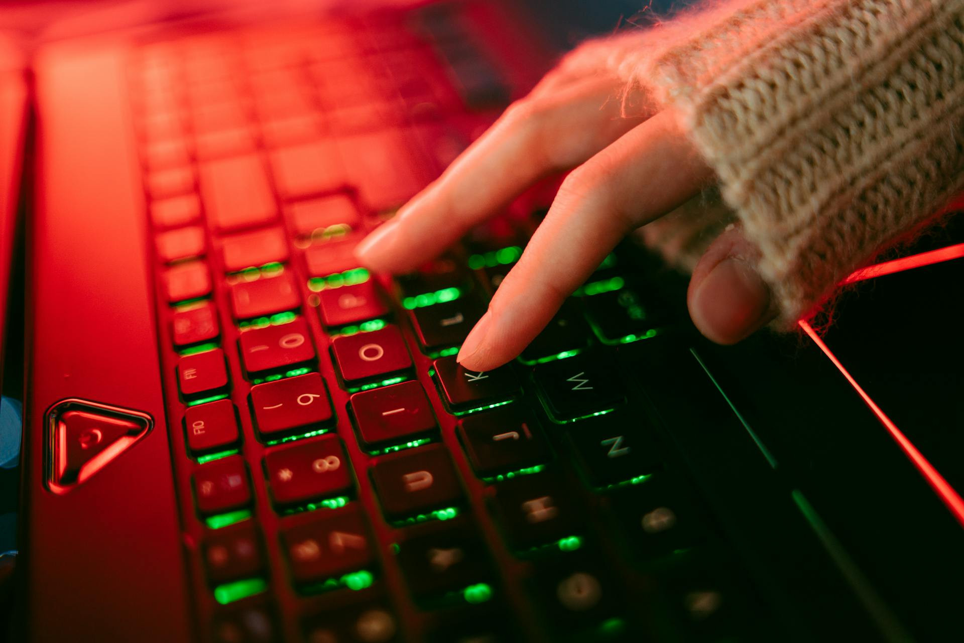 A hand typing on a backlit keyboard in a dark ambiance, highlighting vibrant key illumination.