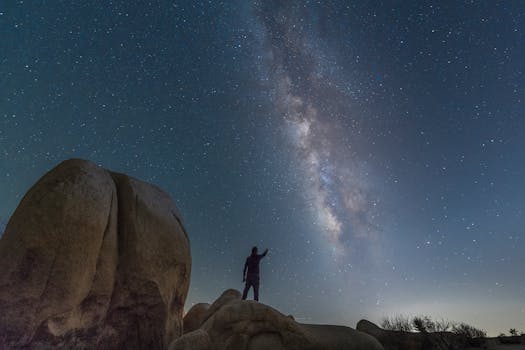 A person silhouetted against the Milky Way starry night in a desert landscape.