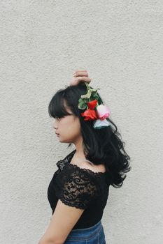 一位时尚的亚洲年轻女性，发间带着花香，在中性色调的粉刷墙壁前展现出别致的优雅