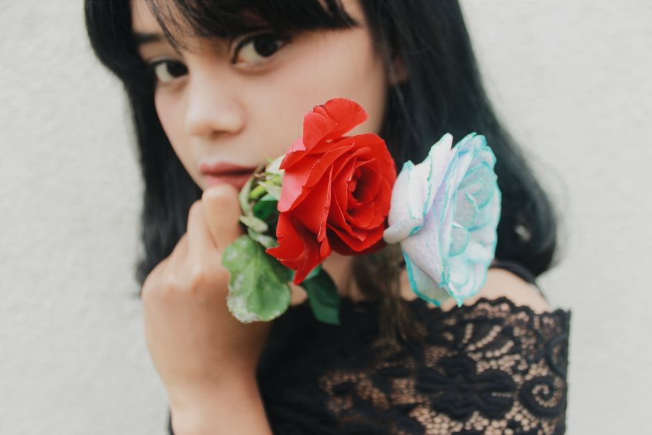 Crop dreamy young ethnic lady with dark hair demonstrating bunch of fresh fragrant roses and looking at camera