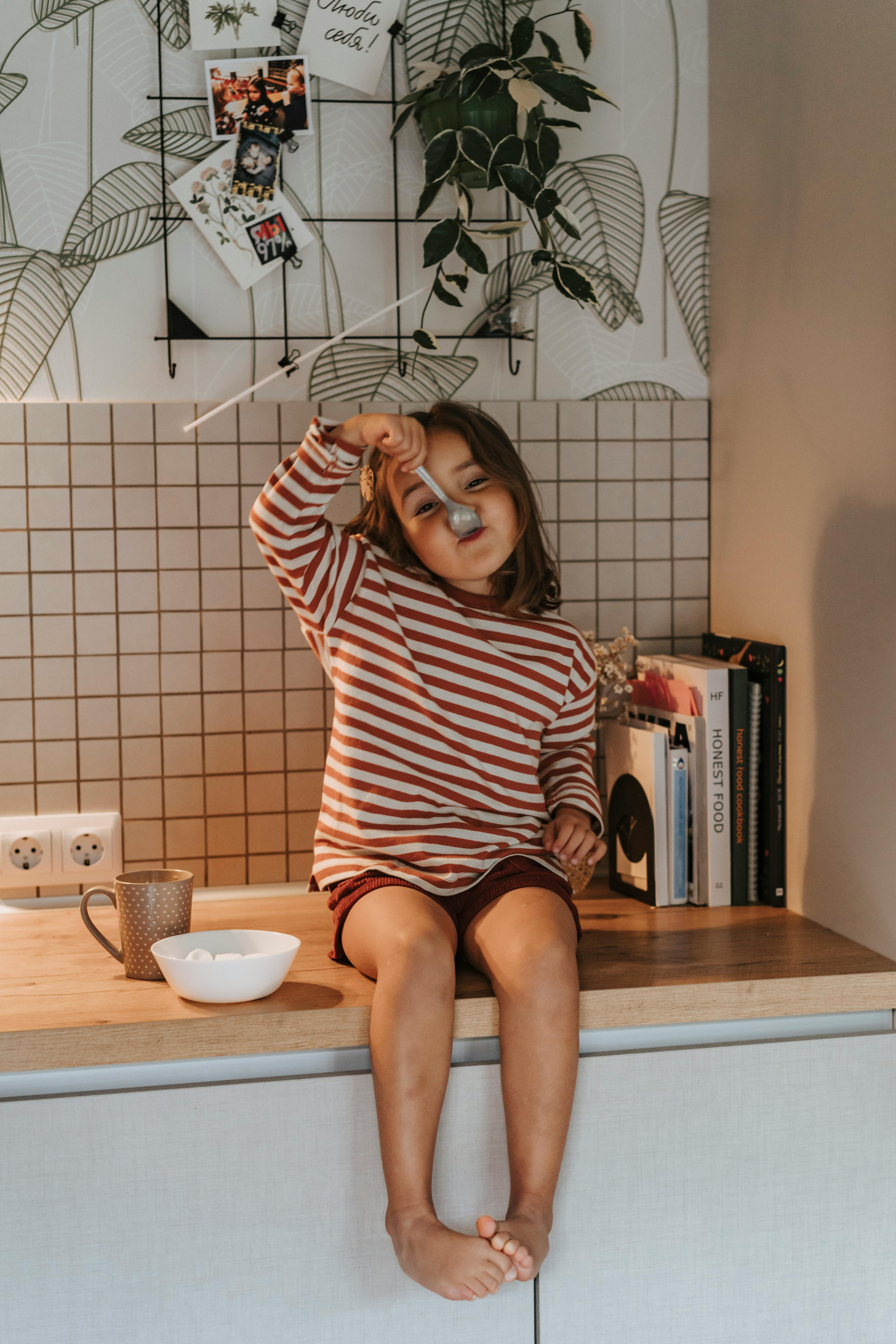 a young girl in striped long sleeves sitting on a wooden table top