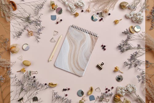 A Notebook Surrounded with Dried Flowers and Metal Binder Clip 