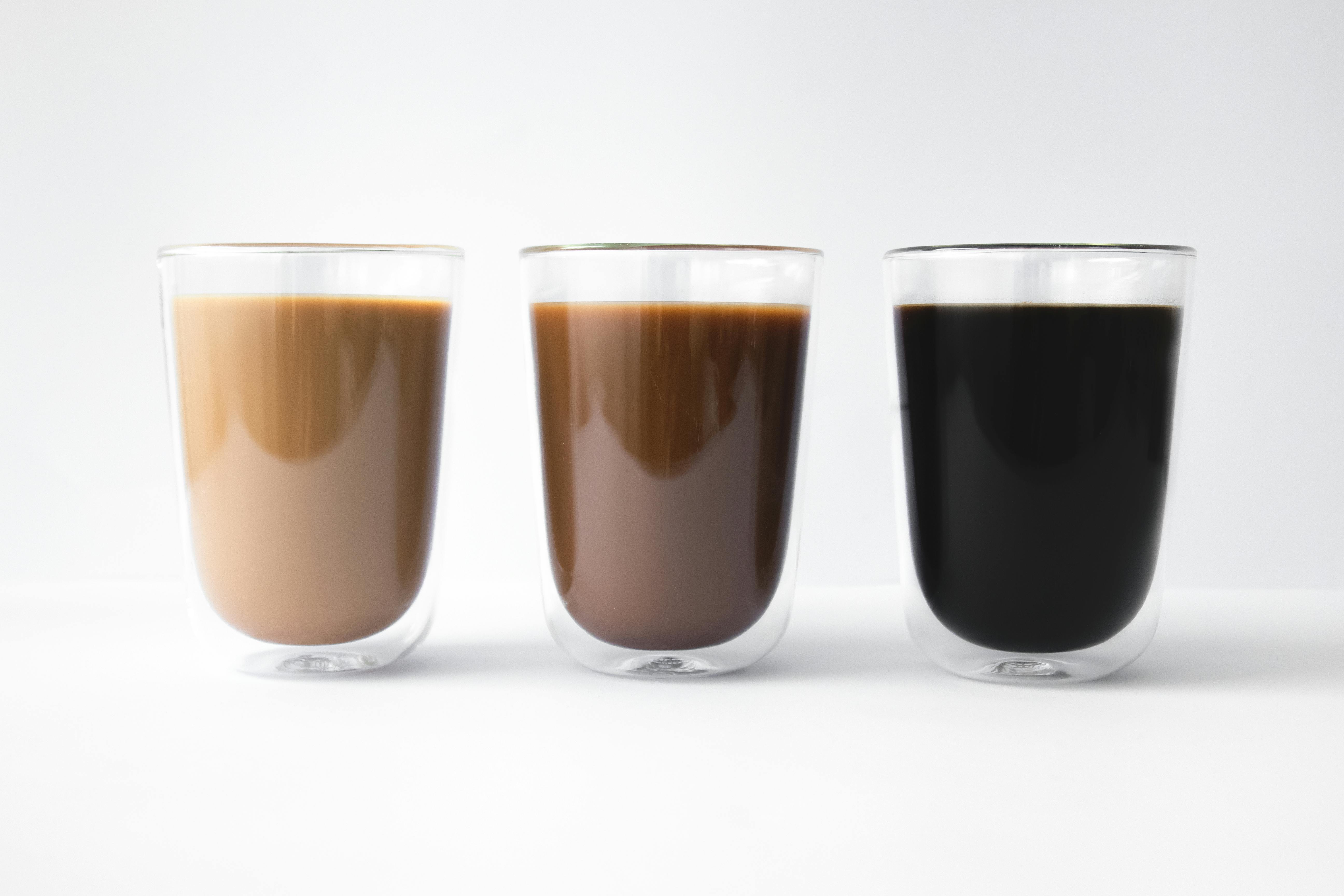 Three glass cups with varying coffee shades in a minimalist setting.