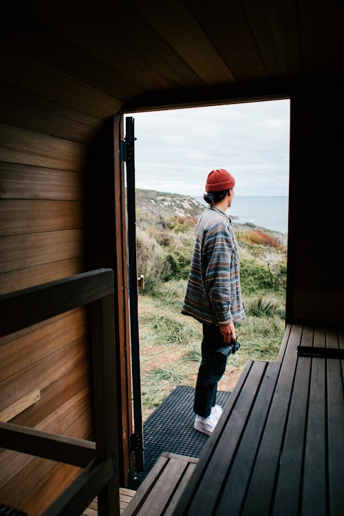 Full body side view of unrecognizable person standing near opened trailer on coast while admiring seascape during trip in nature