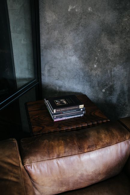 From above stack of books placed on brown leather pouf in stylish room with gray wall and mirror with reflection