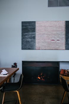 Modern fireplace with burning firewood in cozy room with wooden table and chairs and creative decoration on wall at home