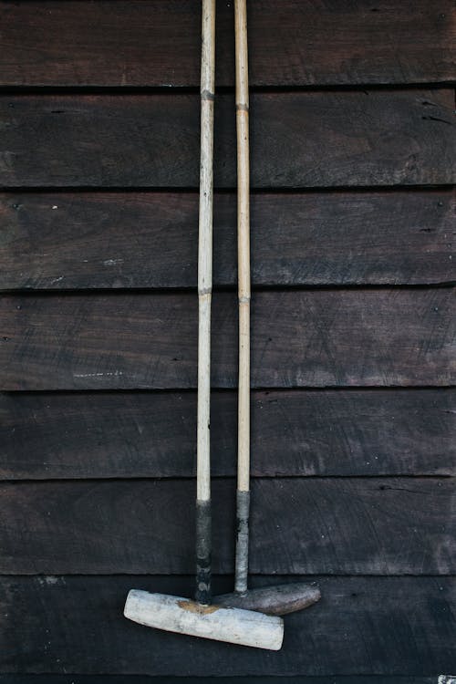 Gardening instruments with long handles hanging on shabby wall with wooden boards on shabby barn in suburb terrain in countryside