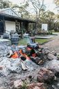 Stone fire pit with burning firewood placed on courtyard of residential building with chairs and table on terrace in countryside