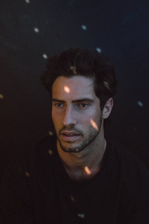 Serious young ethnic man looking away in dark studio