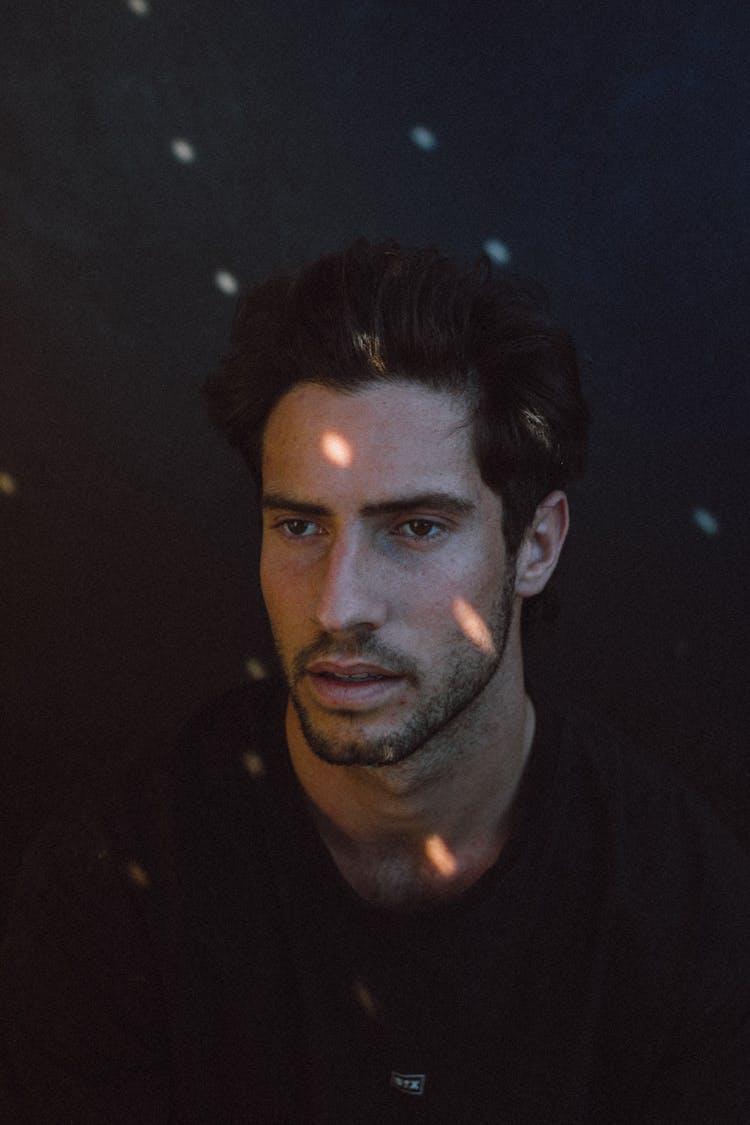 Serious Young Ethnic Man Looking Away In Dark Studio