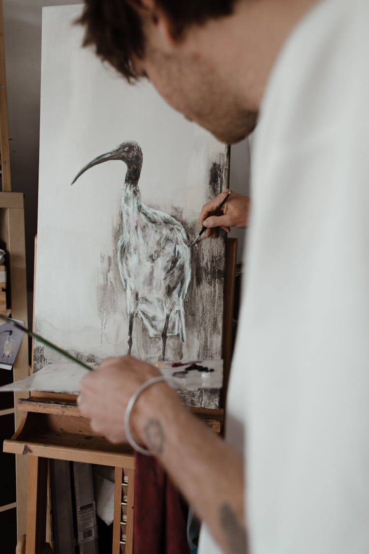 Crop Concentrated Young Male Painter Drawing Bird On Easel In Workshop