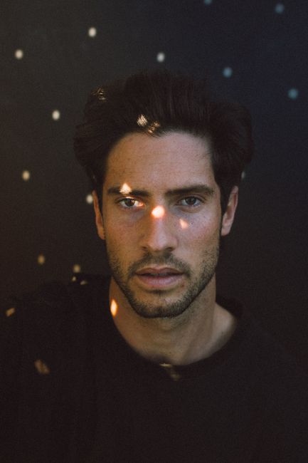 Sun flares on face of serious young unshaven ethnic guy looking at camera against black background