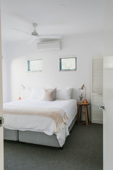 Bed with pillows and blanket placed between wooden bedside tables in spacious bedroom with windows and air conditioner at home