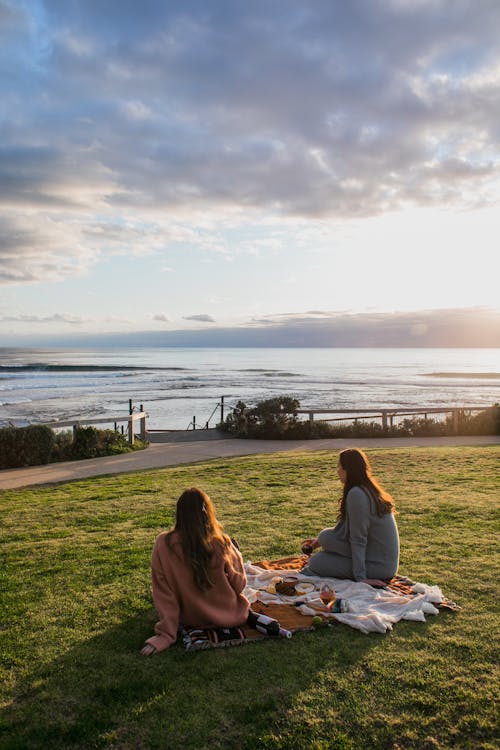 Unrecognizable women having picnic on grassy coast