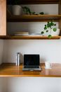 Contemporary netbook with black screen on table with cup of hot drink placed near wooden shelves with flowerpots and book