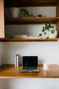 A cozy and contemporary home workspace with a laptop, book, and plants on a wooden desk.
