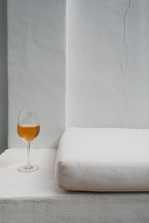 Transparent glass of tasty alcoholic drink near soft clean pillow and white walls