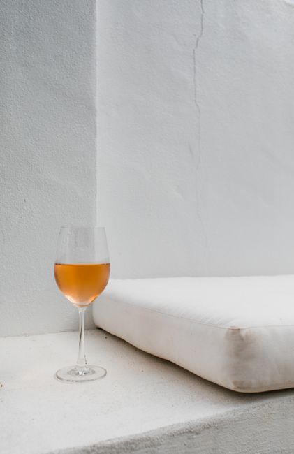 Composition of glass with tasty wine near white comfortable pillow on bed near wall