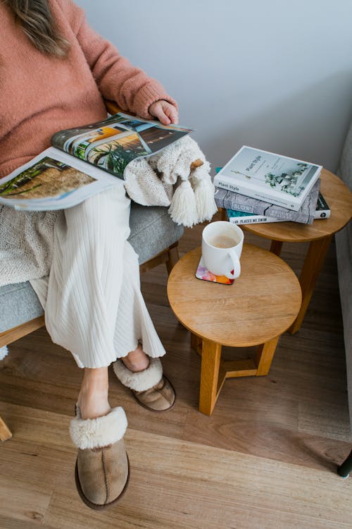 Anonymous lady in armchair reading magazine near table with cup