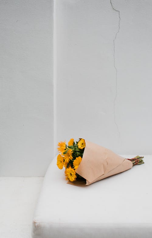 Blooming yellow flowers with gentle petals and pleasant aroma in wrapping paper on white background with crack