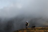 雾气缭绕的山间，一位带着狗的冒险徒步旅行者的剪影被拍摄下来，捕捉到了大自然的宁静