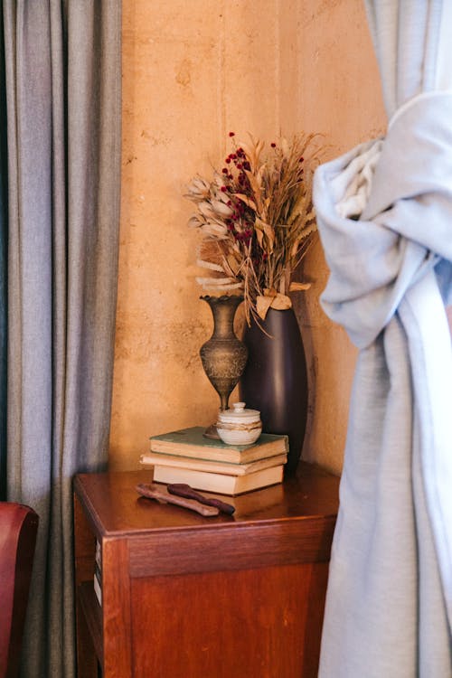 Rustic wooden cabinet with stacked books candleholder and vase place in living room near blue curtains