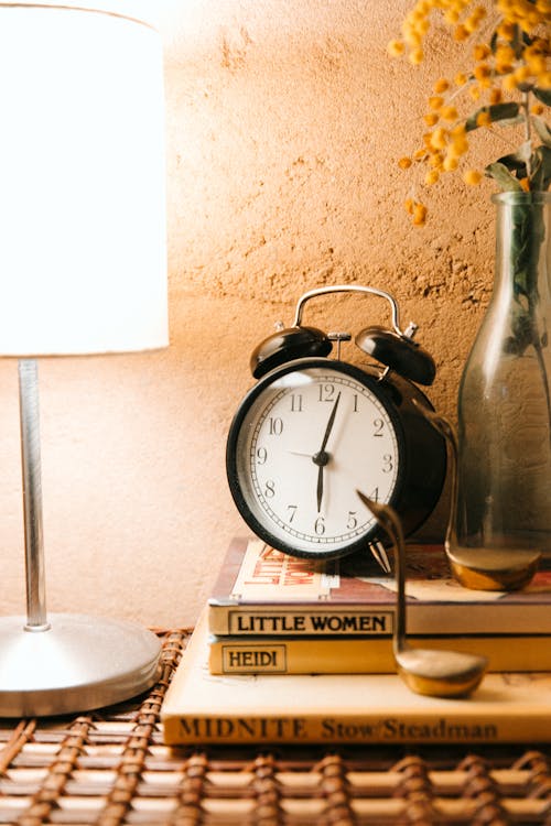 Free Vintage alarm clock and luminous lamp placed on bedside table Stock Photo