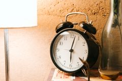 Old fashioned alarm clock placed on stacked books near luminous lamp on bedside table