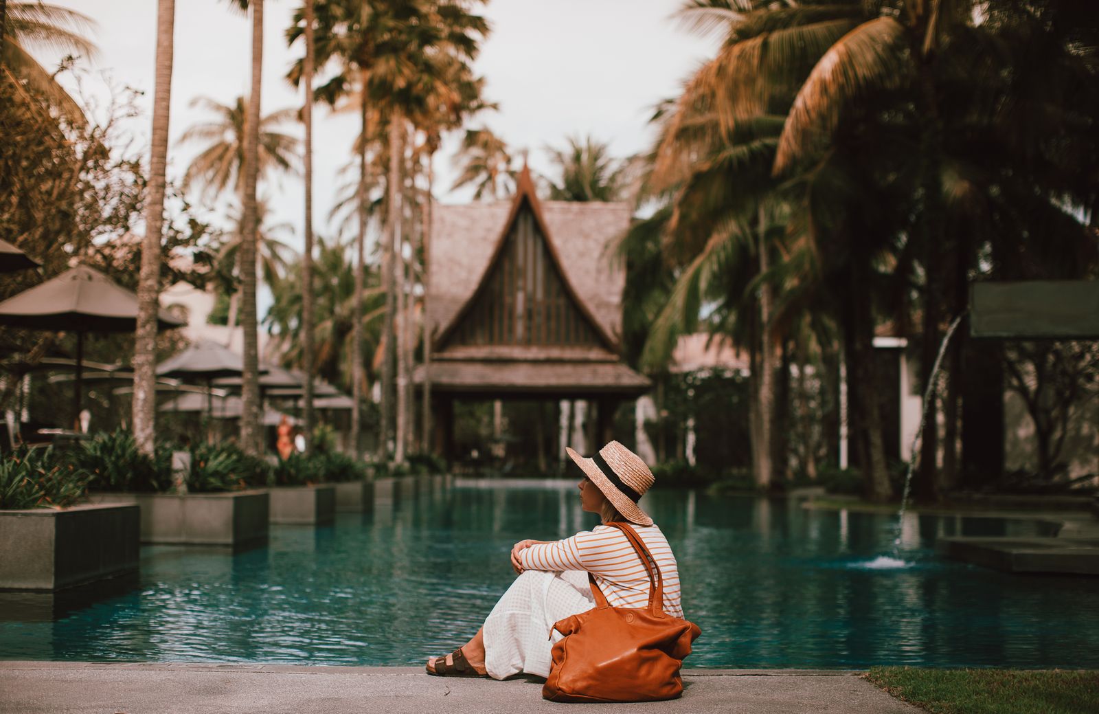 Woman wearing an elegant summer dress beside a luxury tropical resort pool
