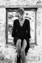 Black and white attractive content female in stylish dress sitting on abandoned grunge building windowsill