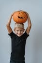 金发男孩脸上带着快乐的微笑，拿着一个雕刻的万圣节南瓜，背景简单