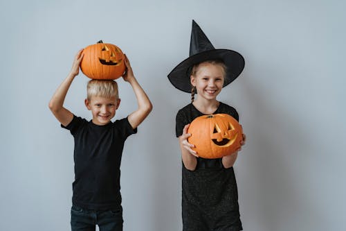 Free Two children in Halloween costumes holding carved pumpkins, smiling and excited for Halloween. Stock Photo