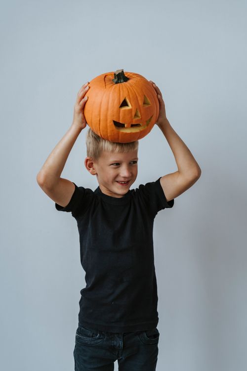 Free A joyful child holds a carved jack-o-lantern against a gray background, celebrating Halloween. Stock Photo