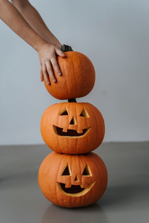 Free Three carved Jack-o'-lanterns stacked on top of each other with a hand adjusting the top pumpkin. Stock Photo