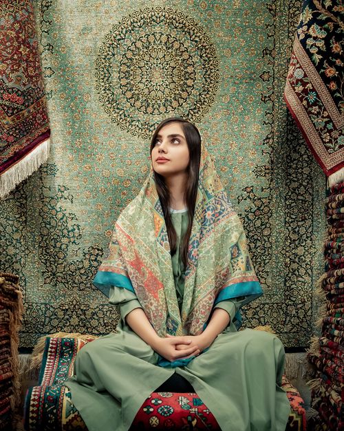 Free A woman in a headscarf sits gracefully among intricate Persian rugs, showcasing traditional craftsmanship. Stock Photo