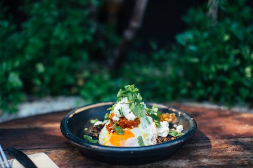 Appetizing fried eggs covered with verdant parsley in plate on timber round shaped table near trees
