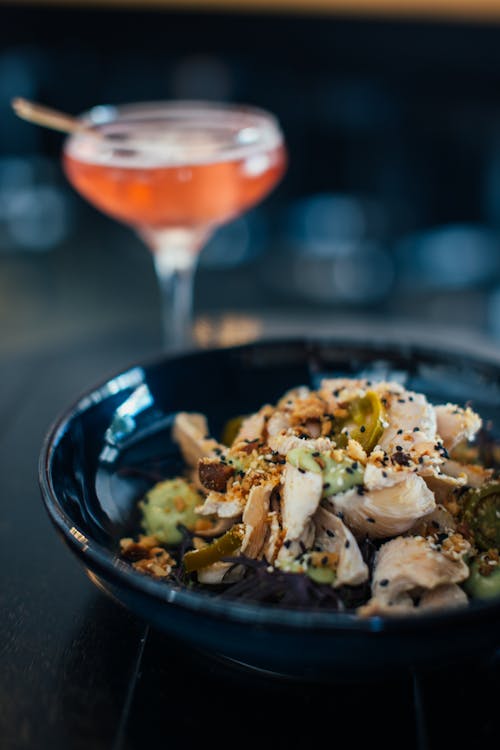 Delicious salad in plate served near glass with sweet alcoholic drink on table on blurred background