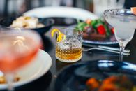 From above glasses of whiskey with ice cubes and lemon peel and vermouth with grapefruit placed on table near assorted dishes in restaurant