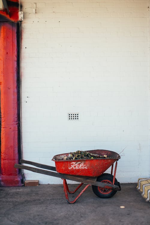 Red metal wheelbarrow cart with soil placed on porch of aged residential house