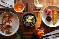 Top view of assorted cocktails and bowl of oysters served on wooden table near plate of fresh raw sliced fish and yummy dessert