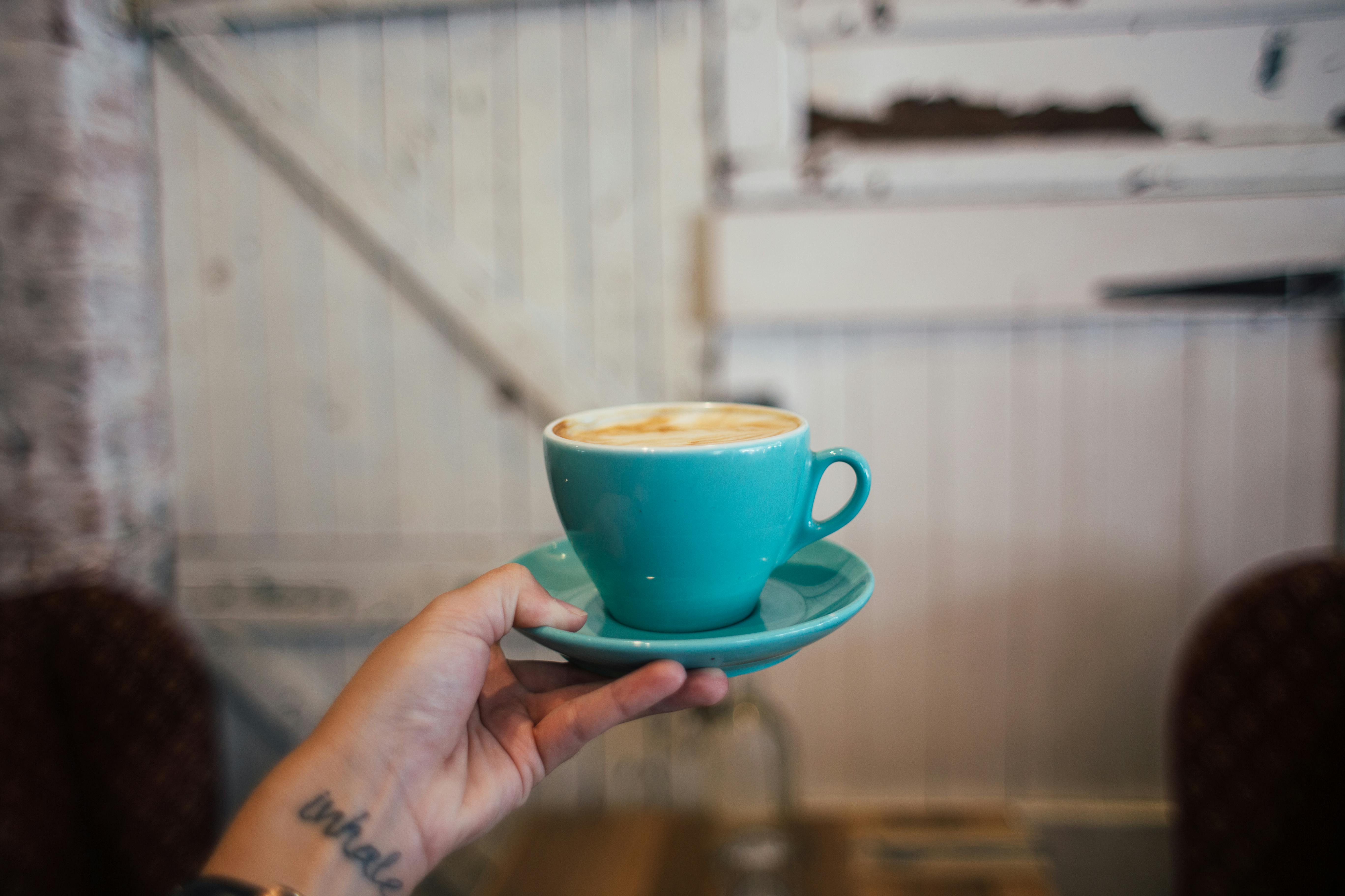 crop woman showing cup of hot cappuccino at home