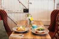 Delicious meals of pancakes with fruits and salad in pita bread with cup of coffee and glass of water on wooden table near big burgundy armchairs