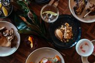 Overhead view of various palatable food including rack of lamb and mashed potatoes with vegetables and piece of cake with water and beer and ice tea surved on wooden table