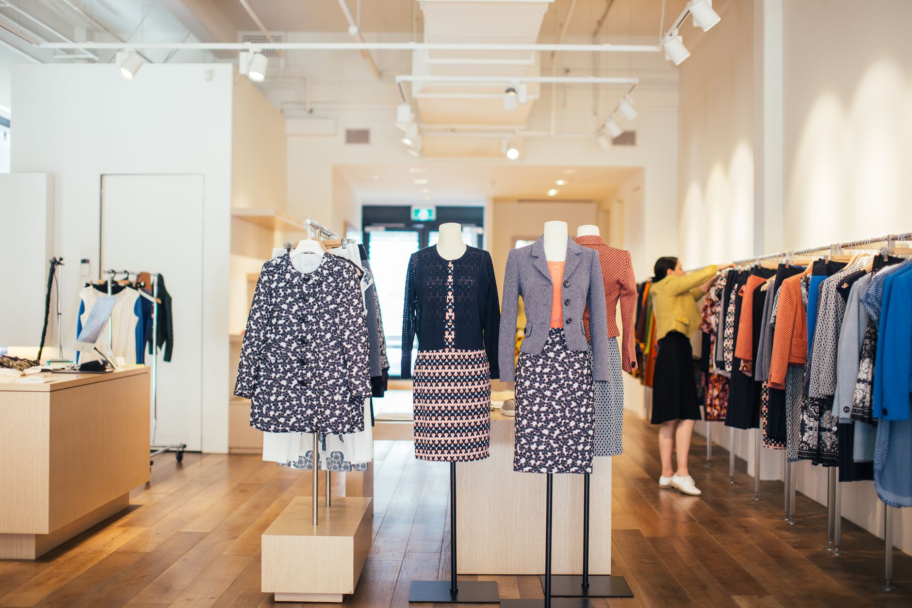 Side view of unrecognizable female seller standing and adjusting stylish colorful clothes hanging on rail in boutique in daytime